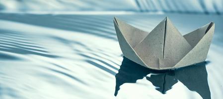 Paper origami boat floating in blue water. Photo with copy space.