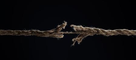 A stretched rope breaks on a black background. The concept of divorce. A break in a relationship. photo