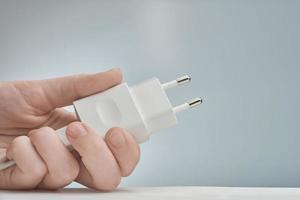 The white electric adapter in a hand, isolated on the gray. photo