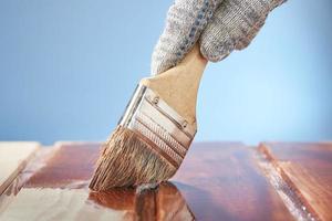 Man's hand with a paint brush painting wooden surface on a blue background. photo