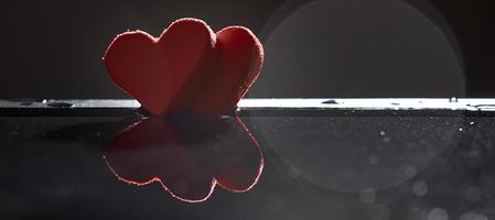 Silhouettes of two red hearts are reflected in the water on a dark background with a bokeh. Photo with copy space.