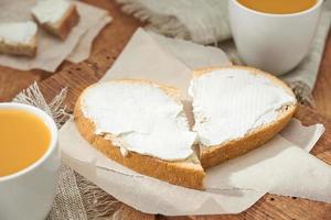 White bread slices with soft butter close up. Breakfast for two sandwiches laid out like a heart, two cups of juice on a wooden table. photo