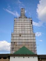 Scaffolding from planks around old bell tower. Background blue sky with clouds. photo