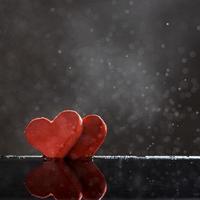 Two red hearts with rain drops reflected in the water on a dark background with a bokeh. Photo with copy space.