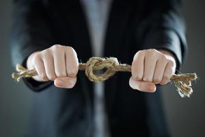 The businessman's hands tighten the rope knot against background of suit in blur.