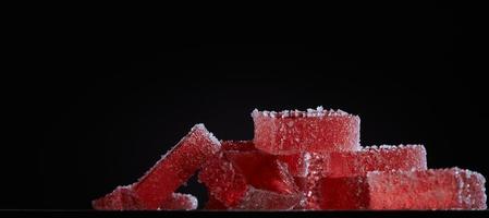 Bright red marmalade jelly candy's on black background. Dessert marmalade in the form of rectangulars. The sweetness of berry jelly candy. Photo with copy space.