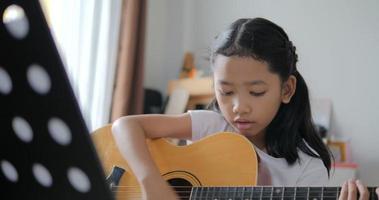 Father teaching to Asian little girl learning to play basic guitar by using electric guitar for beginner music instrumental self studying at home video