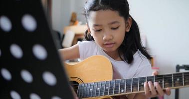 Father teaching to Asian little girl learning to play basic guitar by using electric guitar for beginner music instrumental self studying at home video