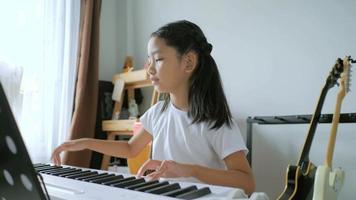 Asian little girl learning to play basic piano by using electric synthesizer keyboard for beginner music instrumental self studying at home video