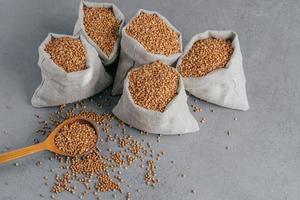 Nutritious ingredient containing vitamins. Shot of linen sacks with buckwheat against grey background. Organic food. Healthy nutrition photo