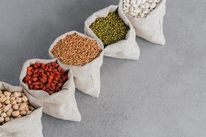 Assorted gluten free grains in linen cloth bags on grey background. Sacks filled with kidney bean, lentil, buckwheat, goji and garbanzo. Cereals for healthy eating photo