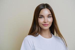 Isolated shot of pleasant looking woman with dark straight hair, wears white t shirt, isolated over brown background, copy space for your advertising content, listens interesting stories and good news photo