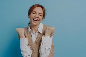 Young happy satisfied young red haired woman with closed eyes celebrating success photo