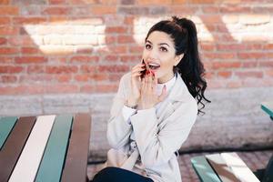 Portrait of surprised beautiful woman with dark pony tail sitting at cafe chatting with her best friend over smartphone gossiping having shocked look after hearing interesting and intriguing news photo