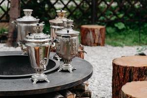 Four metalic samovars outdoor and wooden stumps around. Cozy atmosphere for tea drinking. Ancient times in Russia photo