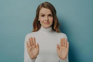 Attractive young focused woman showing stop gesture, saying no, isolated over blue studio background photo