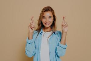 Positive lady with fingers crossed on beige background photo