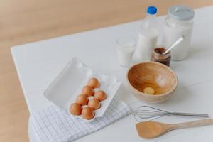 ingredientes de cocina en la mesa de la cocina. vista desde arriba de huevos, leche y harina, batidor y espátula de madera cerca. utensilios y productos frescos foto