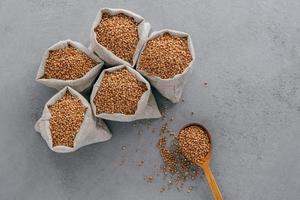 Top view of brown buckwheat in sacks and wooden spoon over grey background. Healthy diet concept. Buckwheat groats. Biologically grown organic plant photo