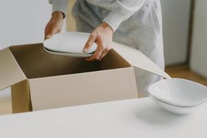 Cropped image of unknown faceless busy man unpacks boxes with dishes, holds white plates, moves in new apartment, tidies up at kitchen, has moving day. Bring out new plates. Relocation concept photo