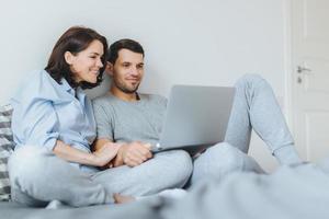Happy couple in love review their wedding photos on laptop computer, remember plesant moments and special event in their life, use modern laptop computer and free internet connection at home
