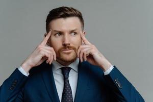 Frustrated businessman in suit holding fingers on temples and looking aside photo