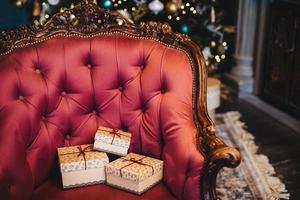 Horizontal picture of wrapped three gift boxes on beautiful royal armchair indoors. Home interior. Celebration, holidays, present concept. Christmas presents decorated with ribbons photo