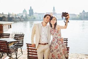 Outdoor shot of happy woman and man embrace each other and pose for making selfie, have stroll near wonderful scenery, being in good mood, enjoys nice weather. People and leisure time concept photo