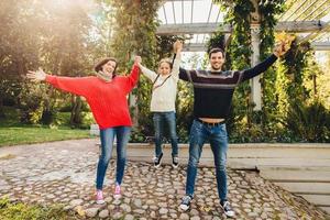 Parents and children concept. Happy family have fun outdoors, female and male play with little kid, swing her in hands, make gestures, have wonderful relationship, enjoy fresh autumn air photo