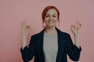 Studio portrait of calm peaceful red-haired business woman with mudra hands gesture photo