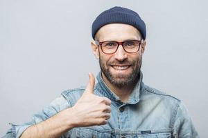 Portrait of glad middle aged male witth thick beard and mustache shows his satisfaction with something, raises thumb, has positive smile on face, isolated over white background. Happiness concept photo