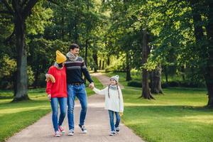 Happy parents feel proud of their small beautiful daughter, have walk together in park, enjoy autumn weather. Family have rest during weekends across green park or forest. Parents and childhood photo