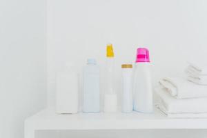 pila de toallas blancas dobladas y botellas con detergente sobre fondo blanco. concepto de lavado y limpieza. espacio para tu texto foto