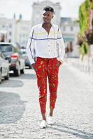 retrato de un apuesto y elegante modelo afroamericano con pantalones rojos y camisa blanca posado en la calle. foto