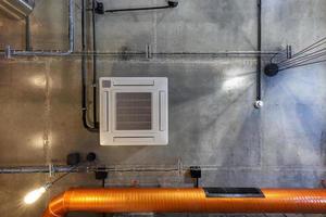 looking up on gray concrete ceiling with halogen spots and edison lamps in loft office room with air conditioning and orange ventilation pipe photo