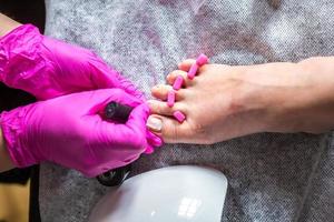 Pedicurist master in pink gloves cuts the cuticle and shellac toe nails in the pedicure salon using drill.  Professional pedicure in cosmetology clinic. Hygiene for feet in beauty salon. photo