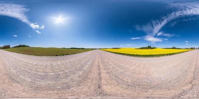 Full spherical seamless panorama 360 degrees angle view on no traffic white sand gravel road among rapeseed fields with cloudy sky in equirectangular projection, VR AR content photo