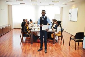 Face of handsome african business man, holding laptop on the background of business peoples multiracial team meeting, sitting in office table. photo