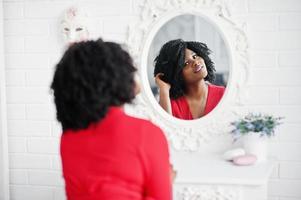 Fashion african american model in red beauty dress, sexy woman posing evening gown and looking at mirror. photo