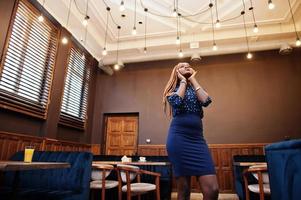 retrato de una hermosa joven mujer de negocios africana con rastas, vestida con blusa azul y falda, posada en un café. foto