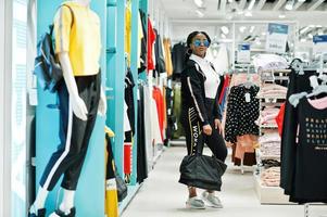 Afican american women in tracksuits and sunglasses shopping at sportswear mall with sport bag against shelves. Sport store theme. photo