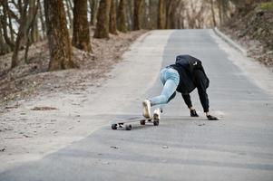 fallar al caer de una patineta. hombre árabe de estilo callejero en anteojos con longboard longboarding por el camino. foto