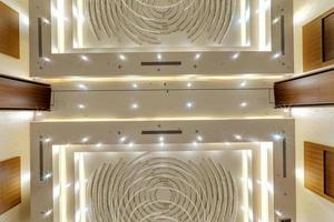 look up on suspended ceiling with halogen spots lamps and drywall construction with fire alarm sensor in empty room in apartment or house. Stretch ceiling white and complex shape. photo