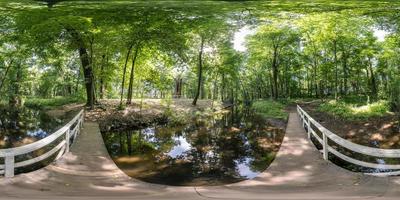 vista de ángulo de 360 grados de panorama hdri esférico completo sobre un puente de madera sobre un pequeño río en el bosque en proyección equirectangular, contenido vr ar. foto