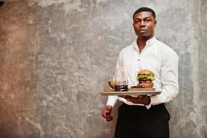 Young african american waiter man hold tray with burger against gray wall. photo