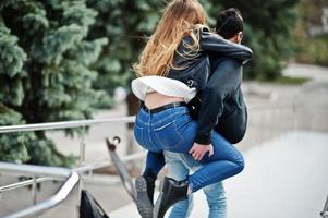 Cool multiracial couple posing with longboard. European girl jumped over shoulder arabian man. photo