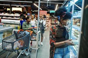 Group of african womans with shopping carts near refrigerator shelf selling dairy products egg carton in the supermarket. photo