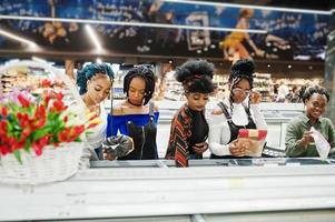 grupo de mujeres africanas con carritos de compras cerca del refrigerador eligen paquetes de albóndigas en el supermercado. foto