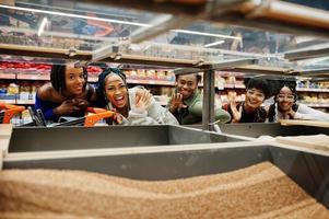 grupo de cinco mujeres africanas divertidas con carritos de compras eligen granos de trigo sarraceno en el supermercado. foto