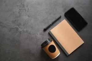 Mock up workspace of smartphone, notebook, take away coffee and pen on dark stone table background with copy space, business and technology concept photo